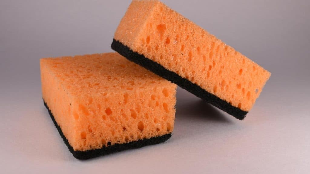 A pair of orange cleaning sponges with black scrubbing surfaces.