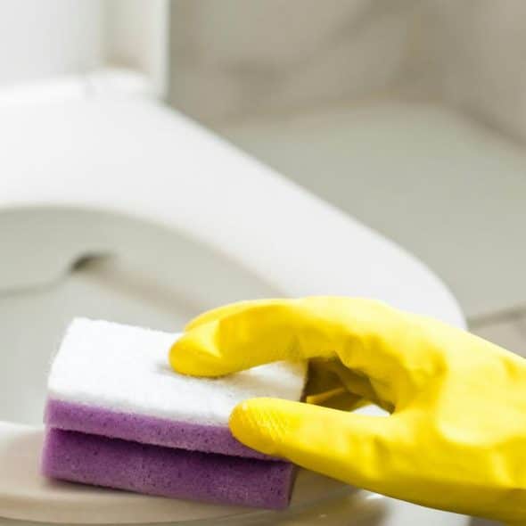 A person's hand in a yellow glove scrubbing a toilet with a sponge.