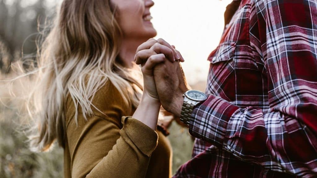 A smiling couple holding hands closely outdoors.
