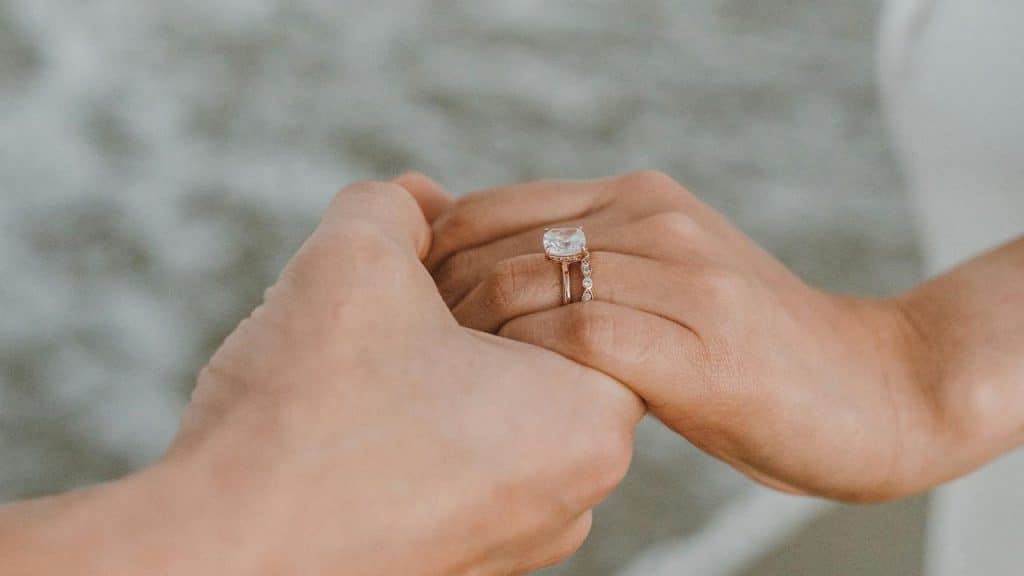 A close-up of two hands holding, with one wearing an engagement and wedding ring set.