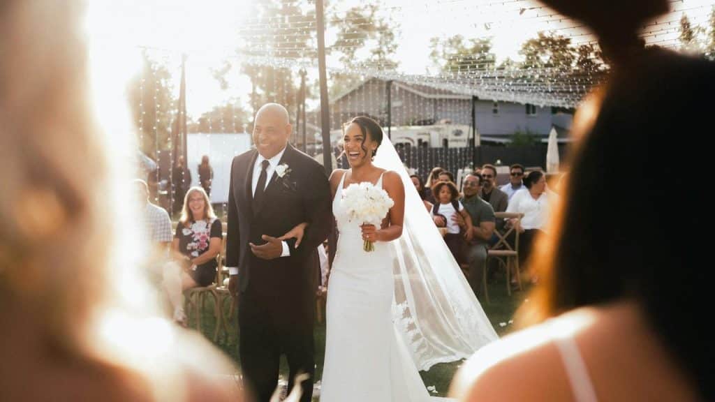 A bride walking down the aisle with a man in a suit at an outdoor wedding.