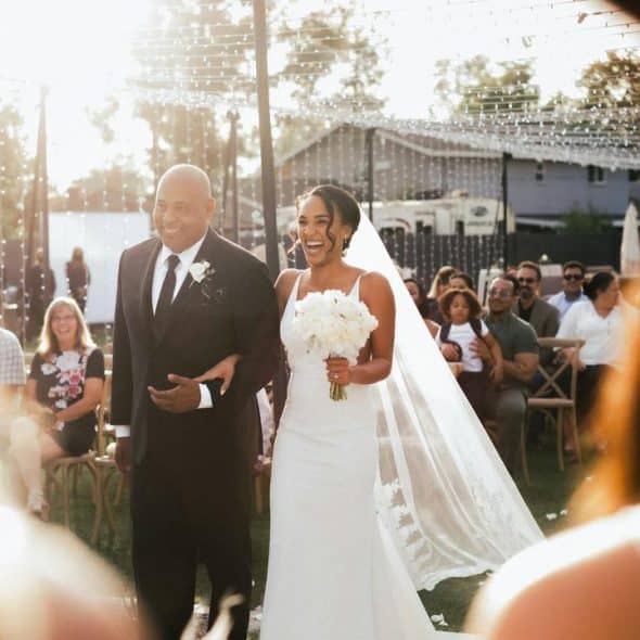 A bride walking down the aisle with a man in a suit at an outdoor wedding.