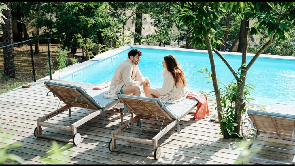 A couple in robes sitting by a pool and holding hands.