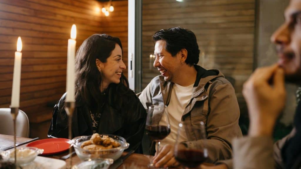 A couple smiling at each other while dining with friends.