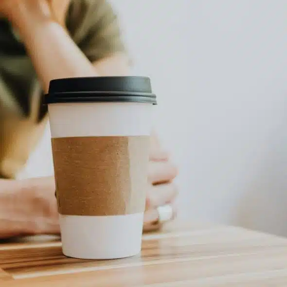 A paper coffee cup displayed on a wooden table with a person sitting behind.
