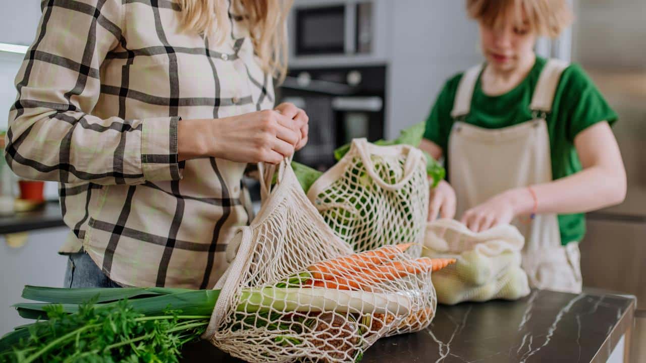 A woman and child unpacking vegetables from reusable mesh bags.