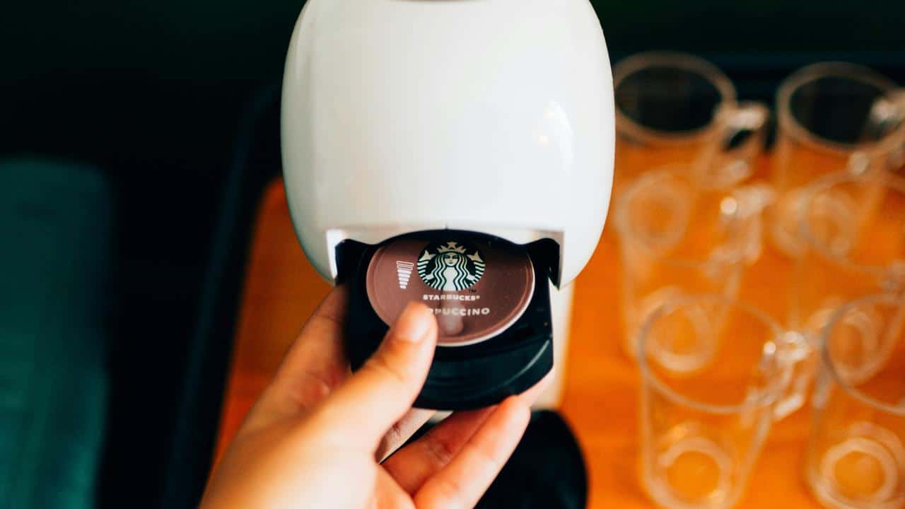 A person's hand placing a Starbucks cappuccino pod into a coffee machine.