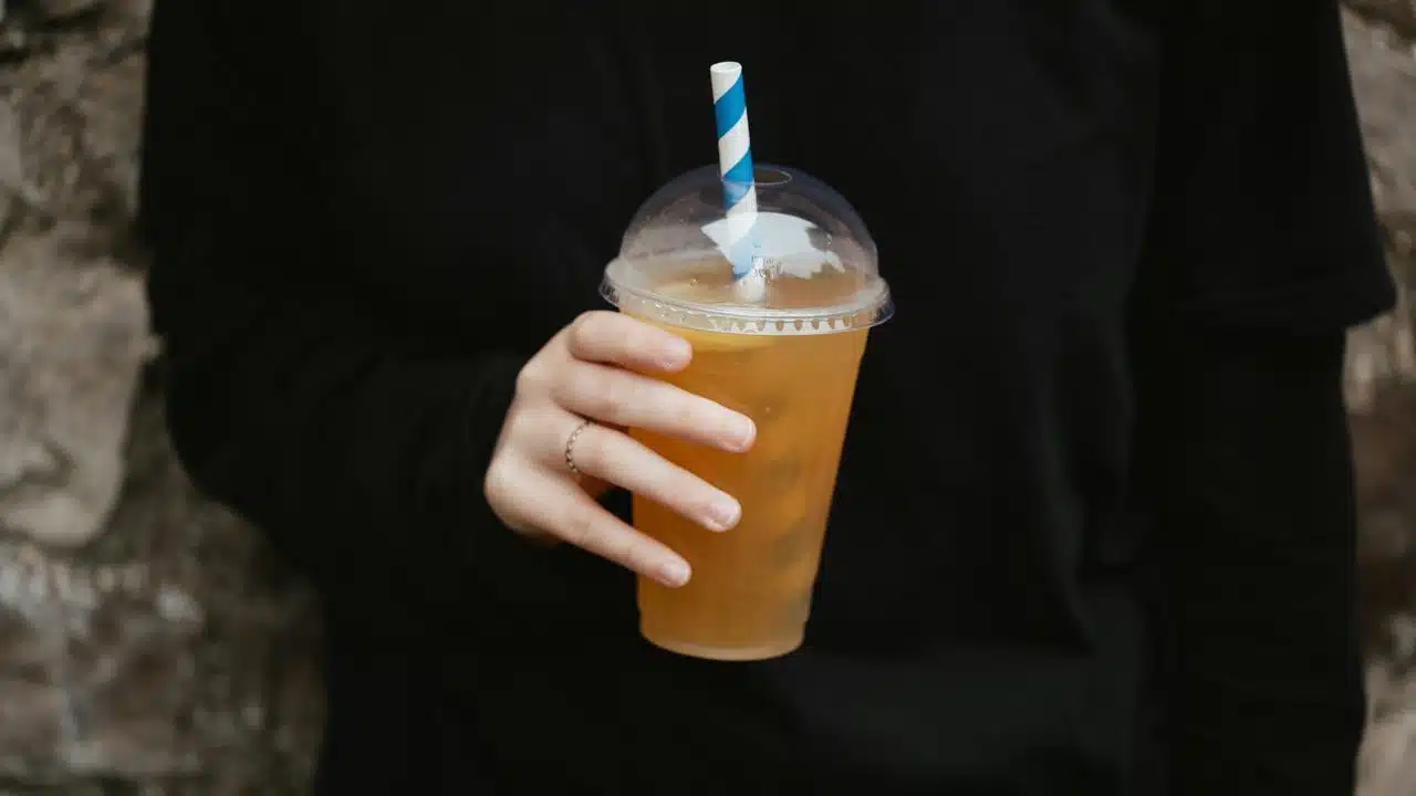 A person holding a plastic cup of iced tea with a striped straw.