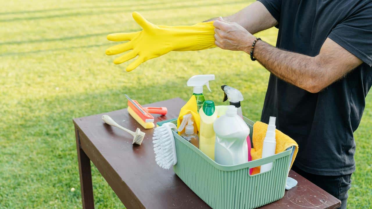 A person putting on yellow cleaning gloves next to cleaning supplies.