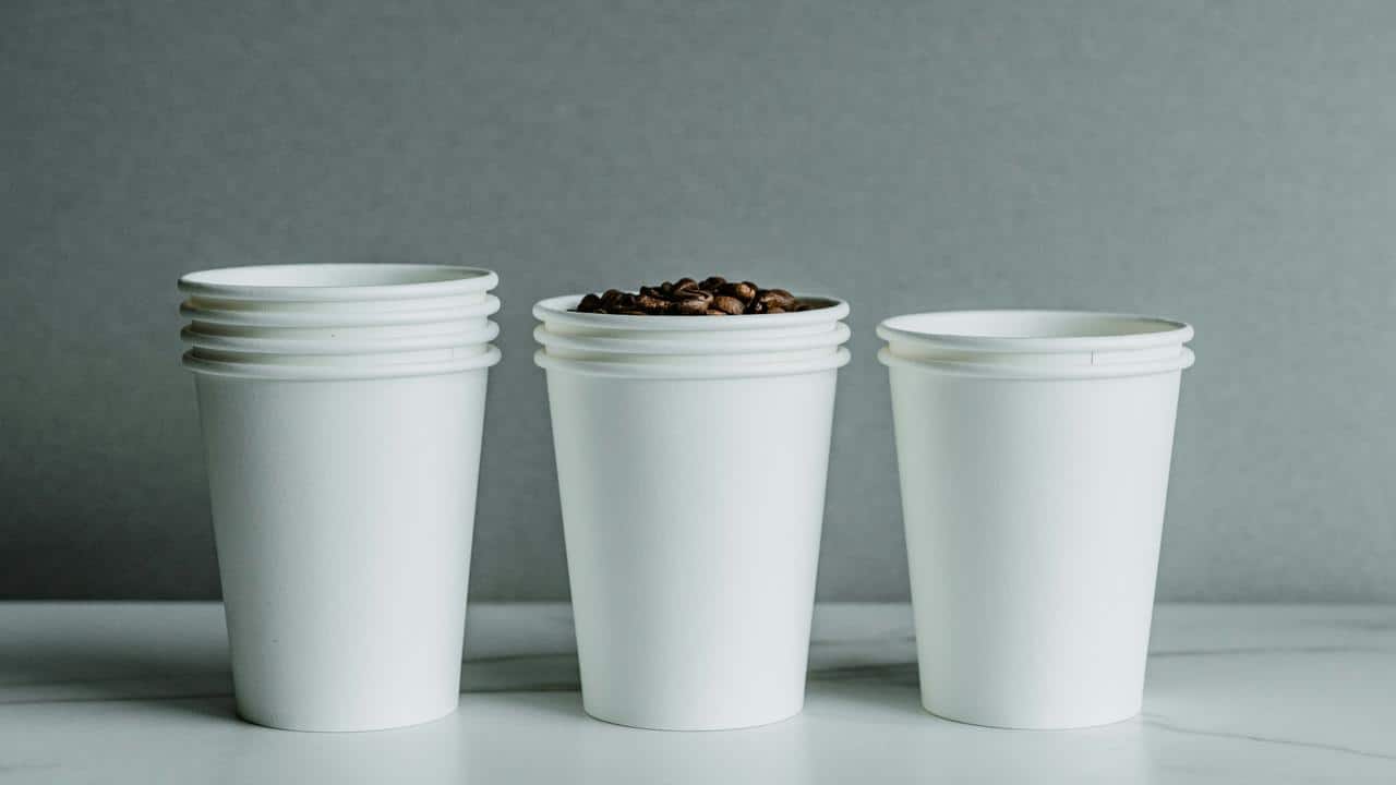 A stack of white paper cups, one filled with coffee beans.