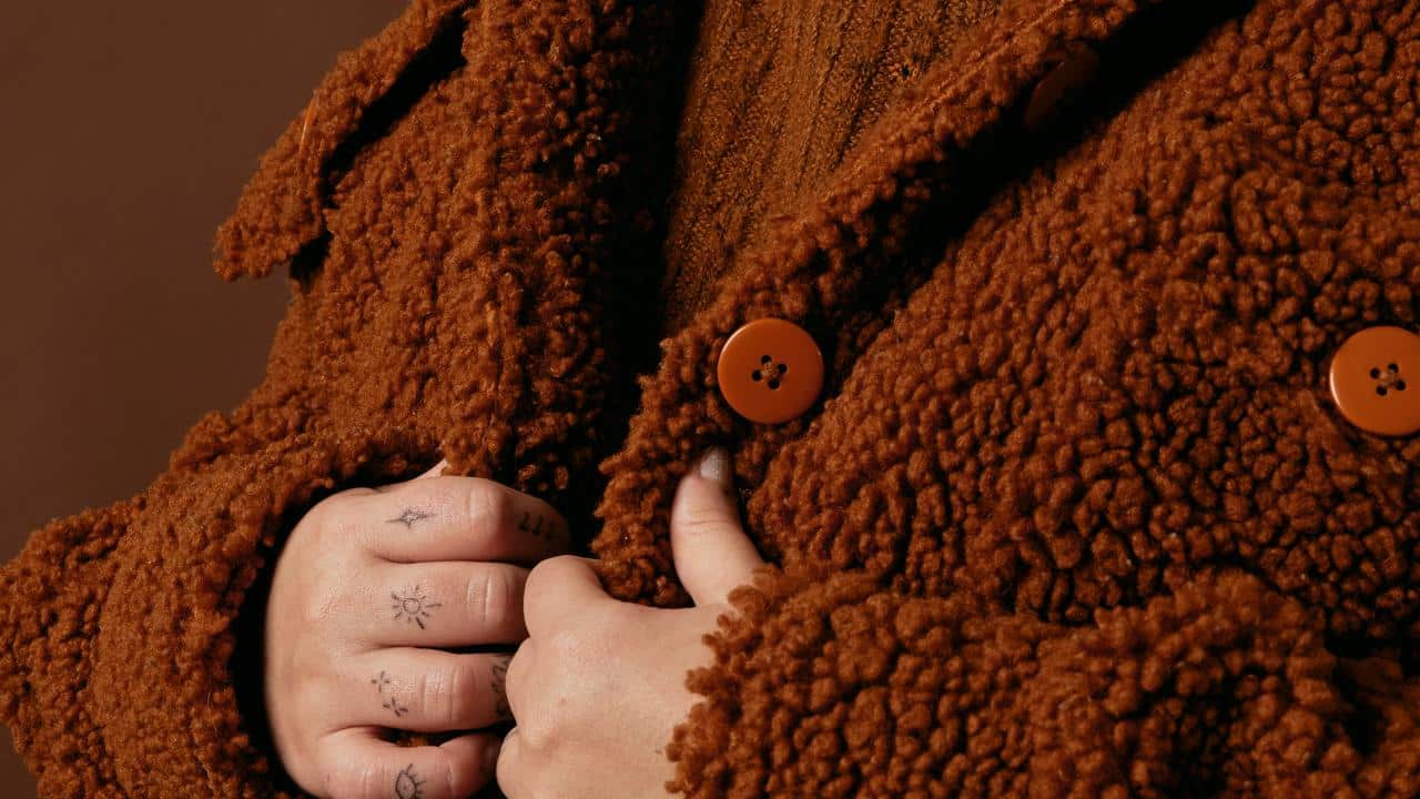 A person wearing a brown textured coat with large buttons.