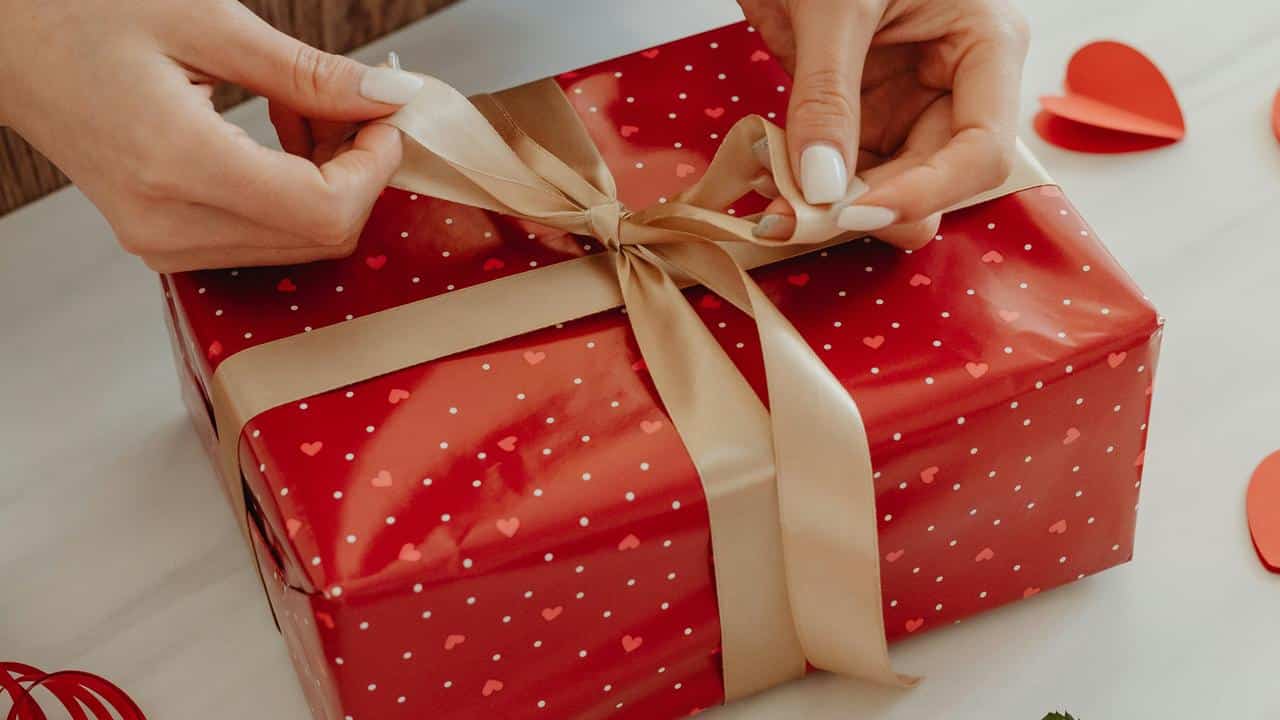 A person tying a ribbon on a red gift box with heart patterns.