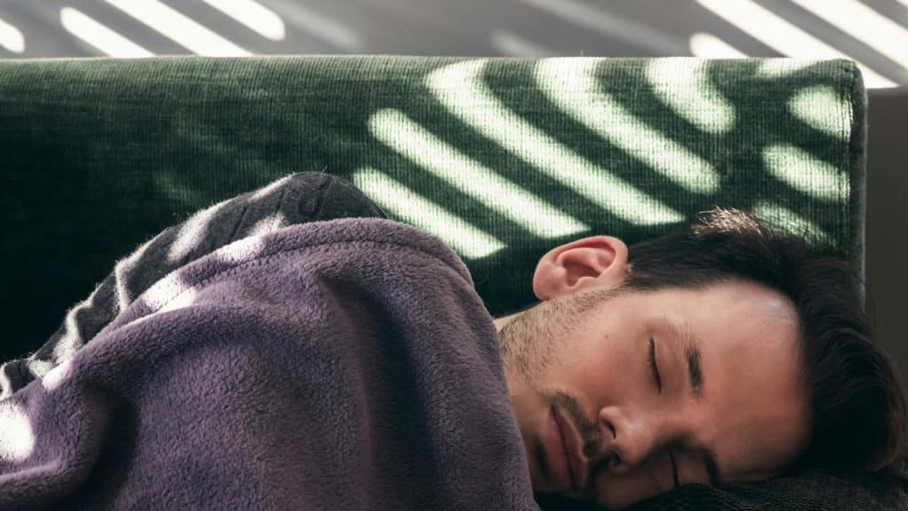 A man sleeping on a couch under a blanket.