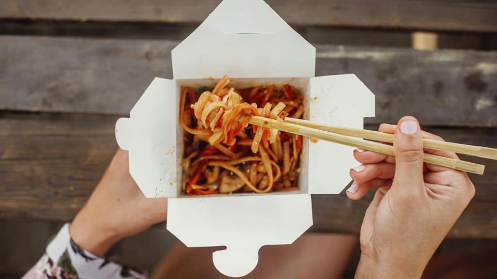 A person eating noodles from a takeout box with chopsticks.
