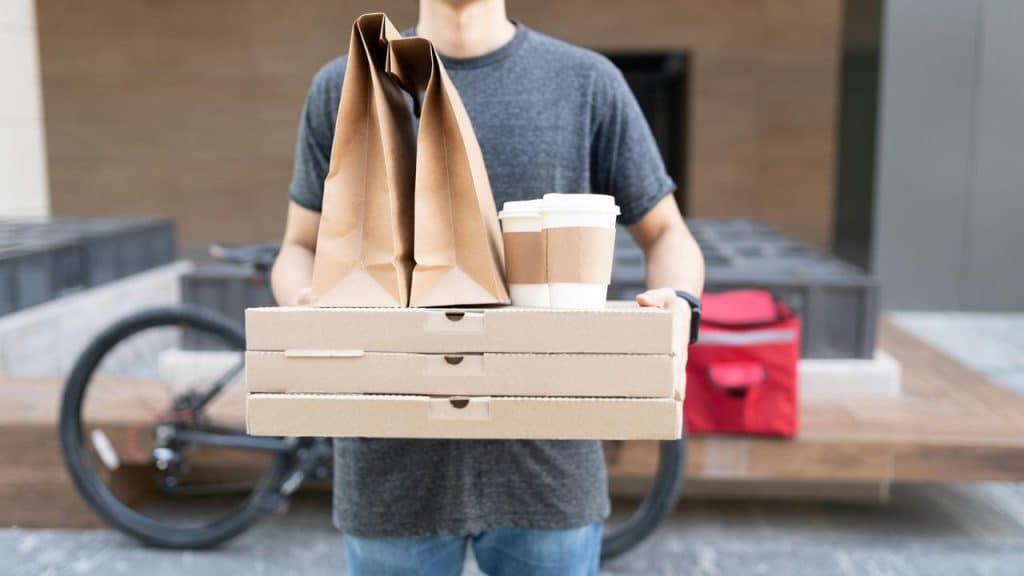 A person holding pizza boxes, paper bags, and coffee cups.