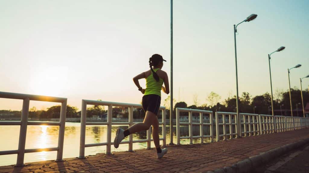 A woman running on the sidewalk with the sunset in the background.