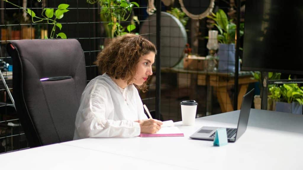 A woman taking notes as she stares at her laptop.