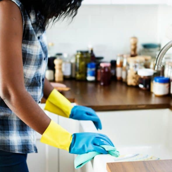 A woman wearing rubber gloves cleaning a kitchen counter.