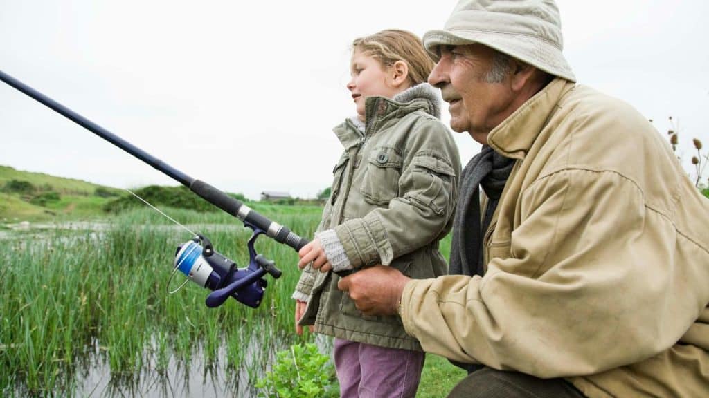 An older man teaching a young child to fish by a pond.