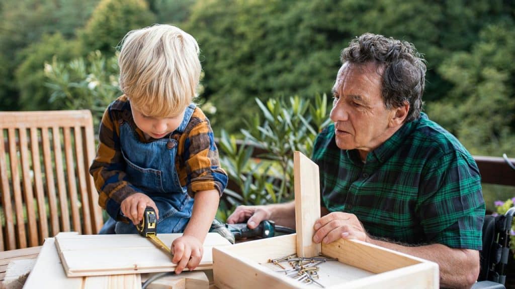 An older man helping a young boy measure wood for a project.