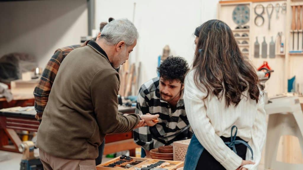An older man showing woodworking tools to a group of younger people in a workshop.