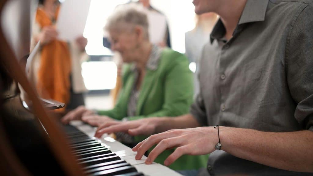 A person playing piano beside an elderly woman in a green jacket.
