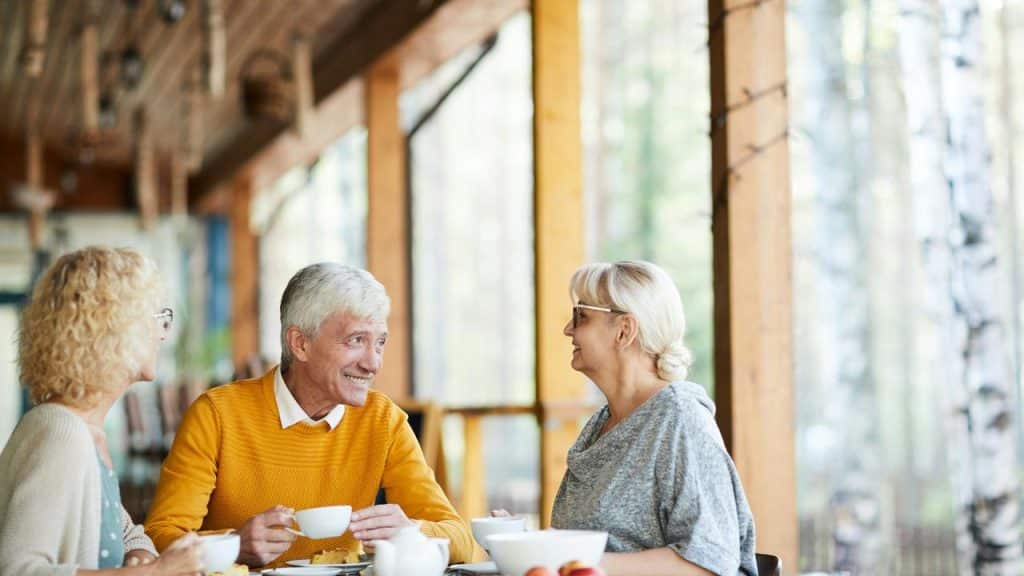 An elderly man and two women talking over coffee at a cafe.