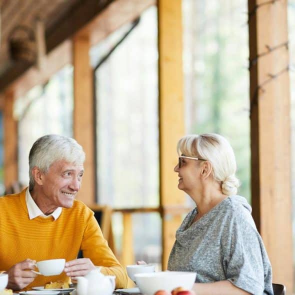 An elderly man and two women talking over coffee at a cafe.