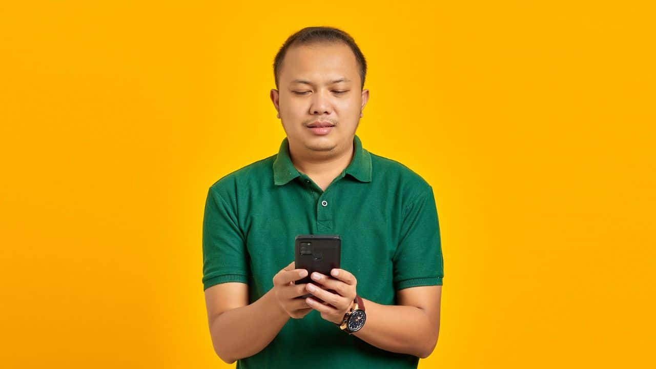 A man in a green shirt is looking down at his phone.