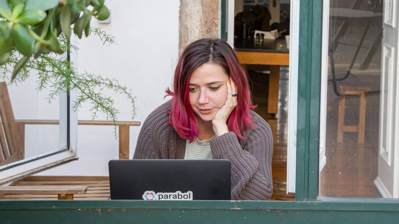 A woman with pink-tipped hair looks intently at her laptop.