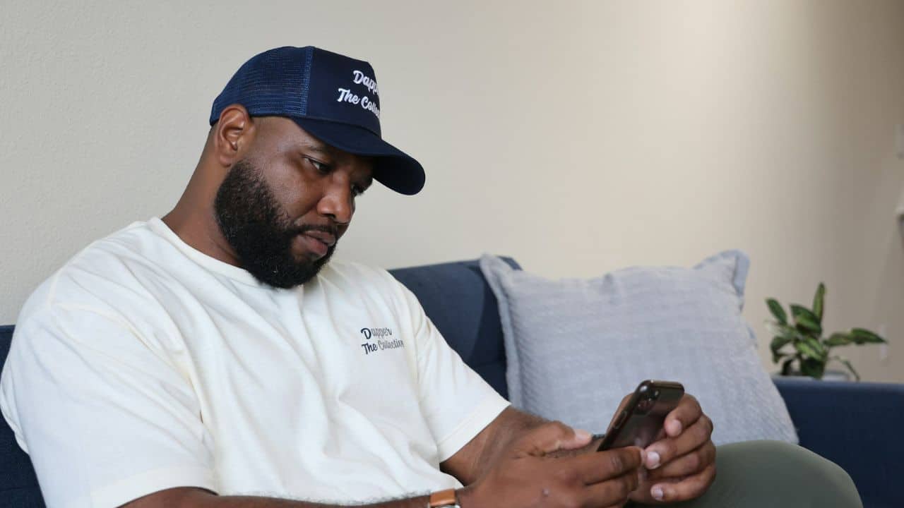A man wearing a baseball cap looks down at his phone.