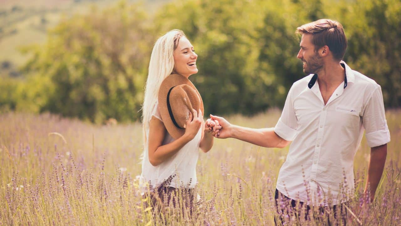A smiling couple holding hands and walking through a field of lavender.
