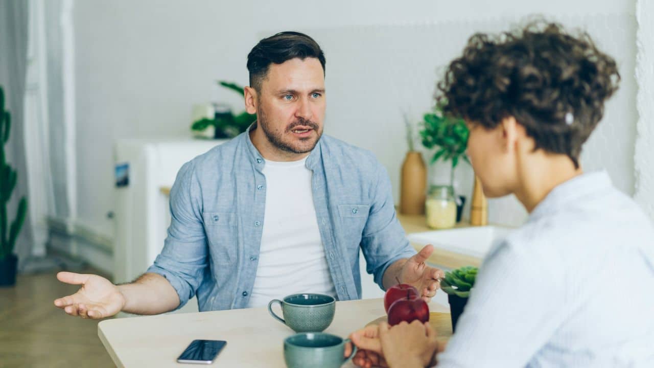 A man with his hands up looks at a woman with a frustrated expression.