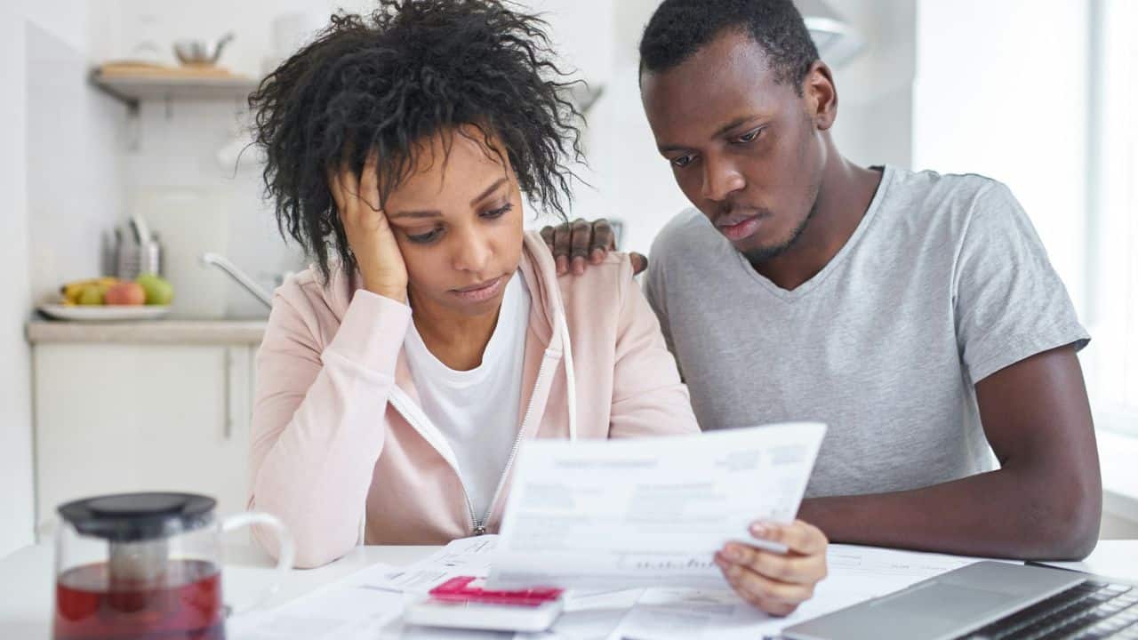 A sad couple sits at a kitchen table looking at bills together.