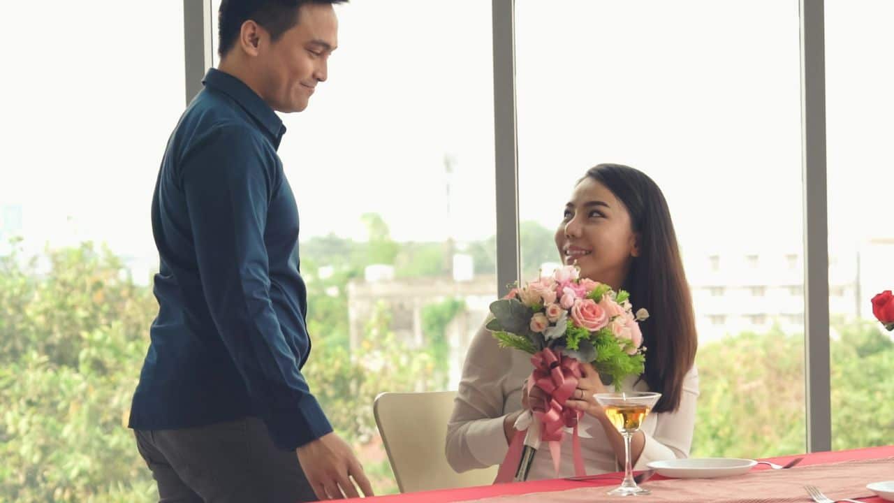 A man gives a bouquet of flowers to a smiling woman at a restaurant.