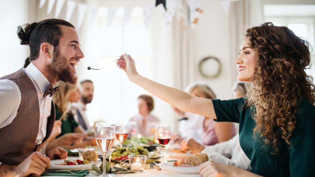 A happy couple at a dinner party feeds each other food.
