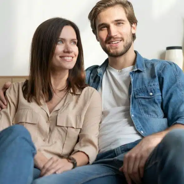A happy, young couple sits closely together on a gray couch.