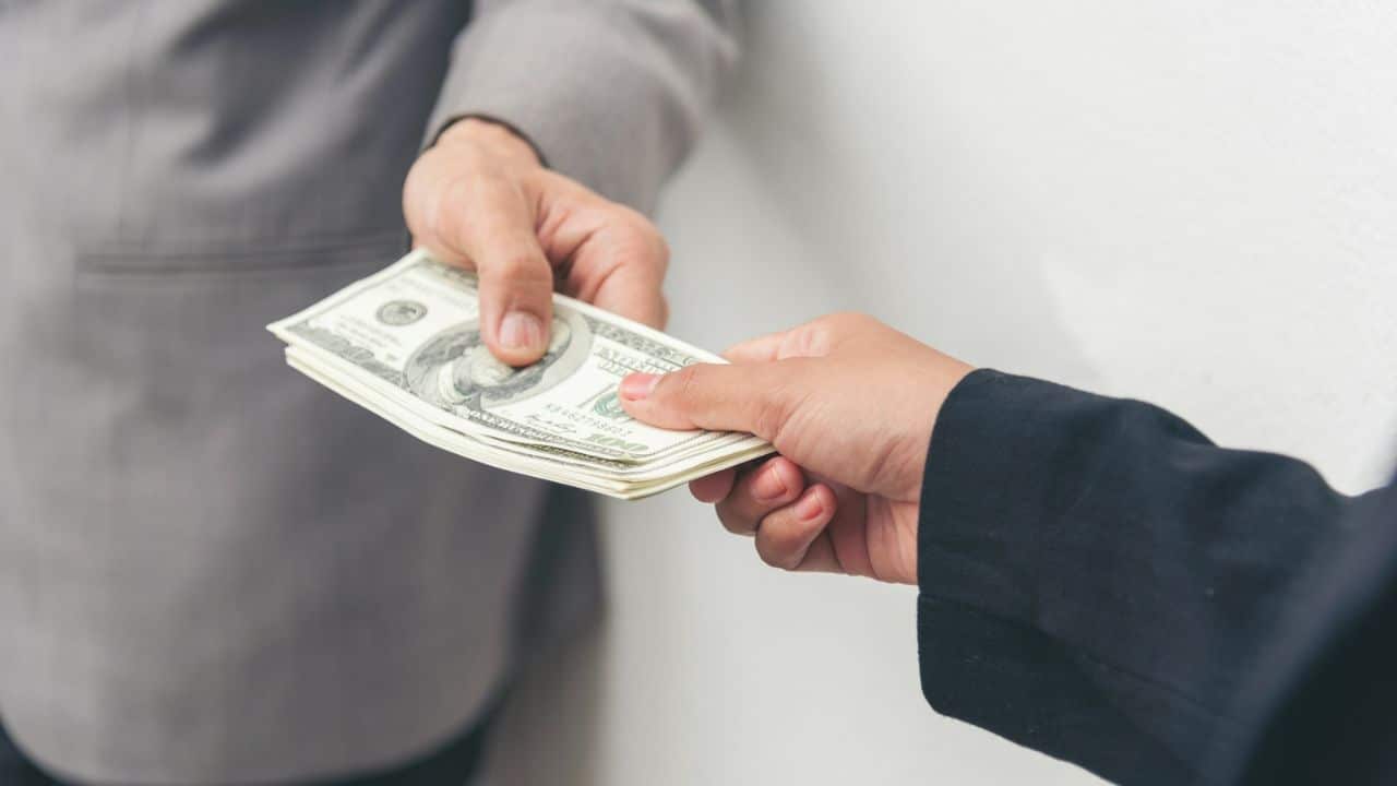 Two people's hands exchanging a stack of U.S. dollar bills.