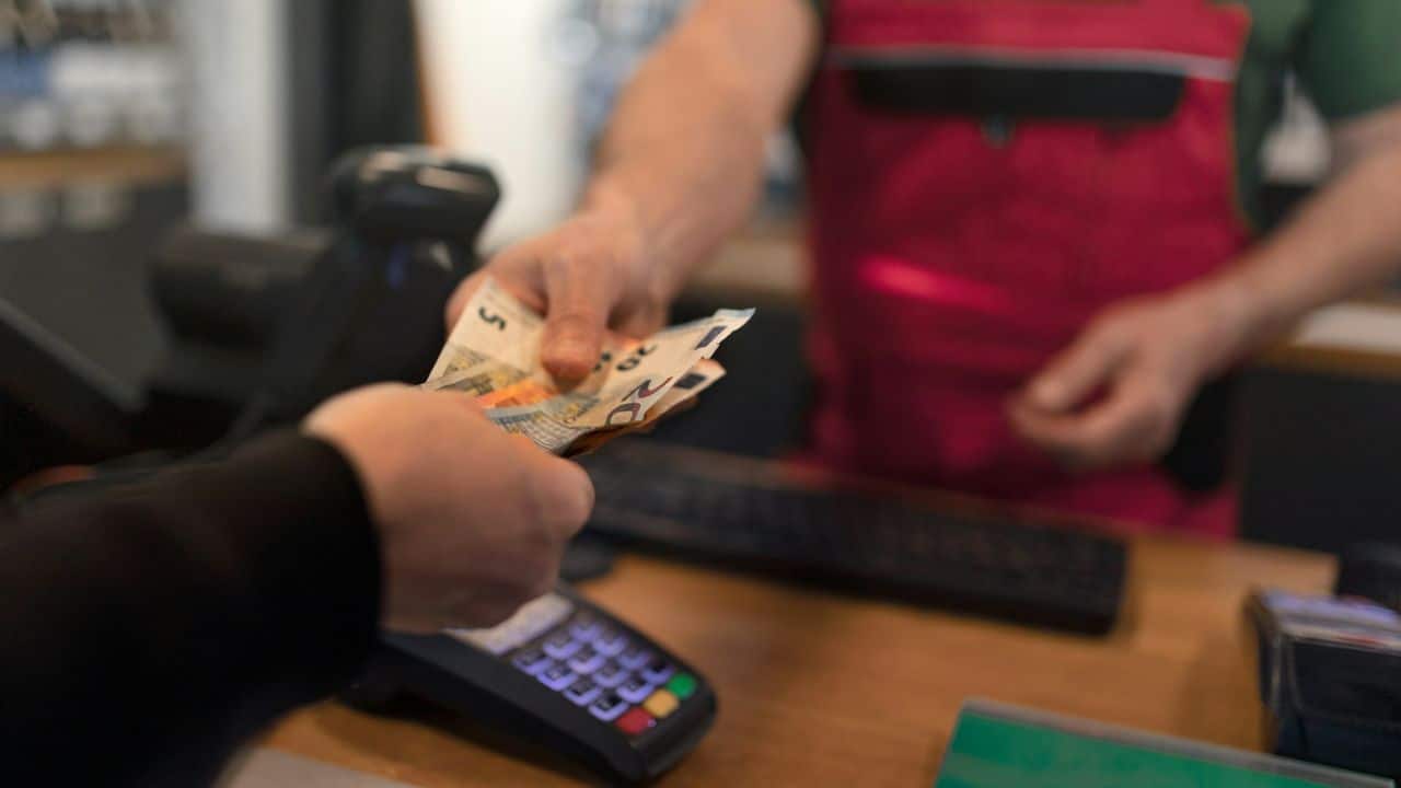 A cashier is receiving euro banknotes from a customer.