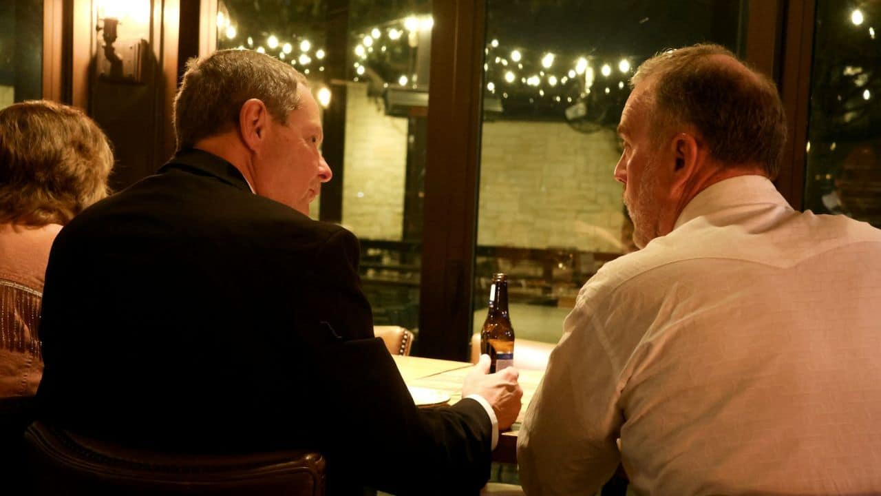 Two men are seated at a table, facing each other and talking.