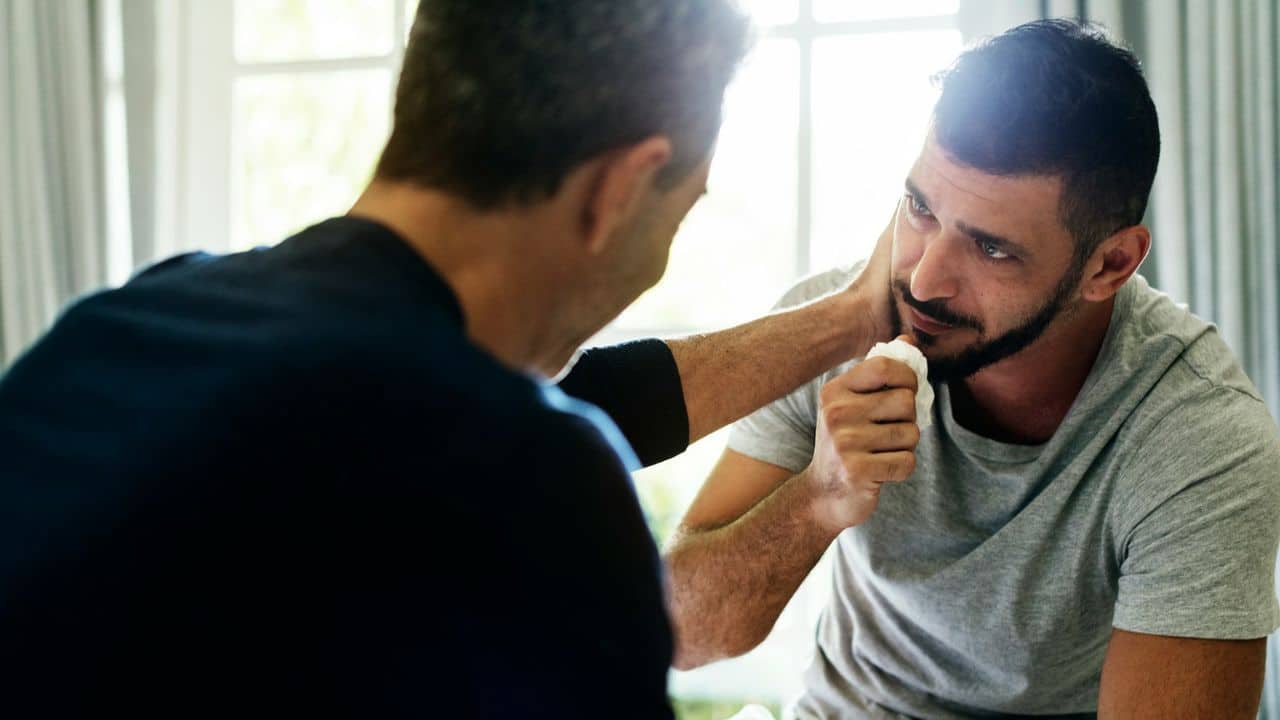 A man is holding a crumpled tissue and is being comforted by another man.