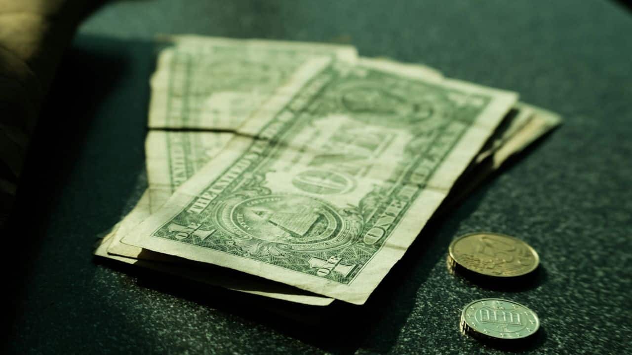 A small stack of American dollar bills and a few coins are lying on a dark surface.
