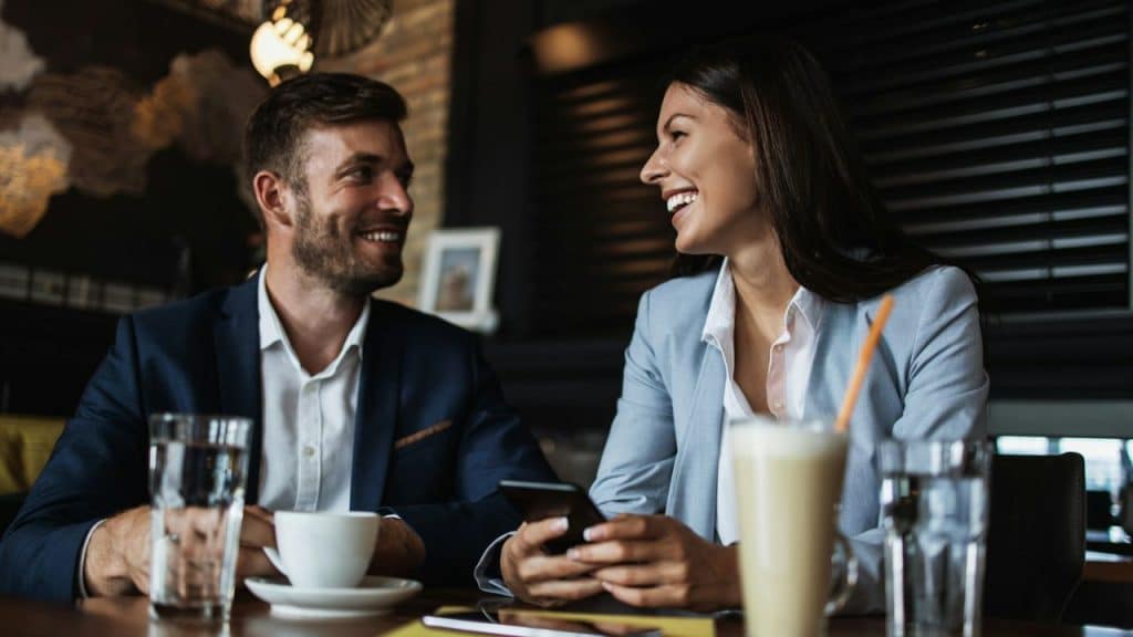 A couple smiles and looks at each other while at a cafe.
