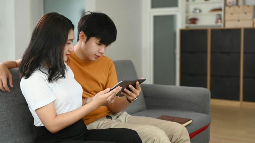 A couple sits on a couch, looking at a tablet together.