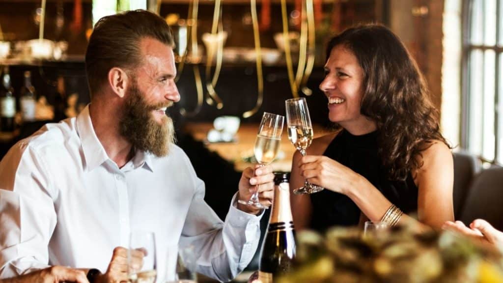A laughing couple toasts with champagne glasses at a dinner table.
