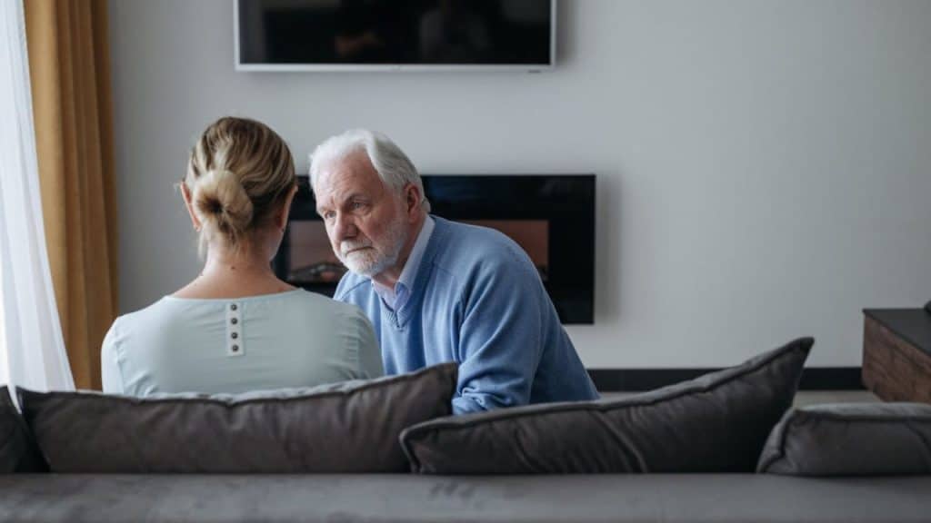 An older couple talks on a couch, facing each other.