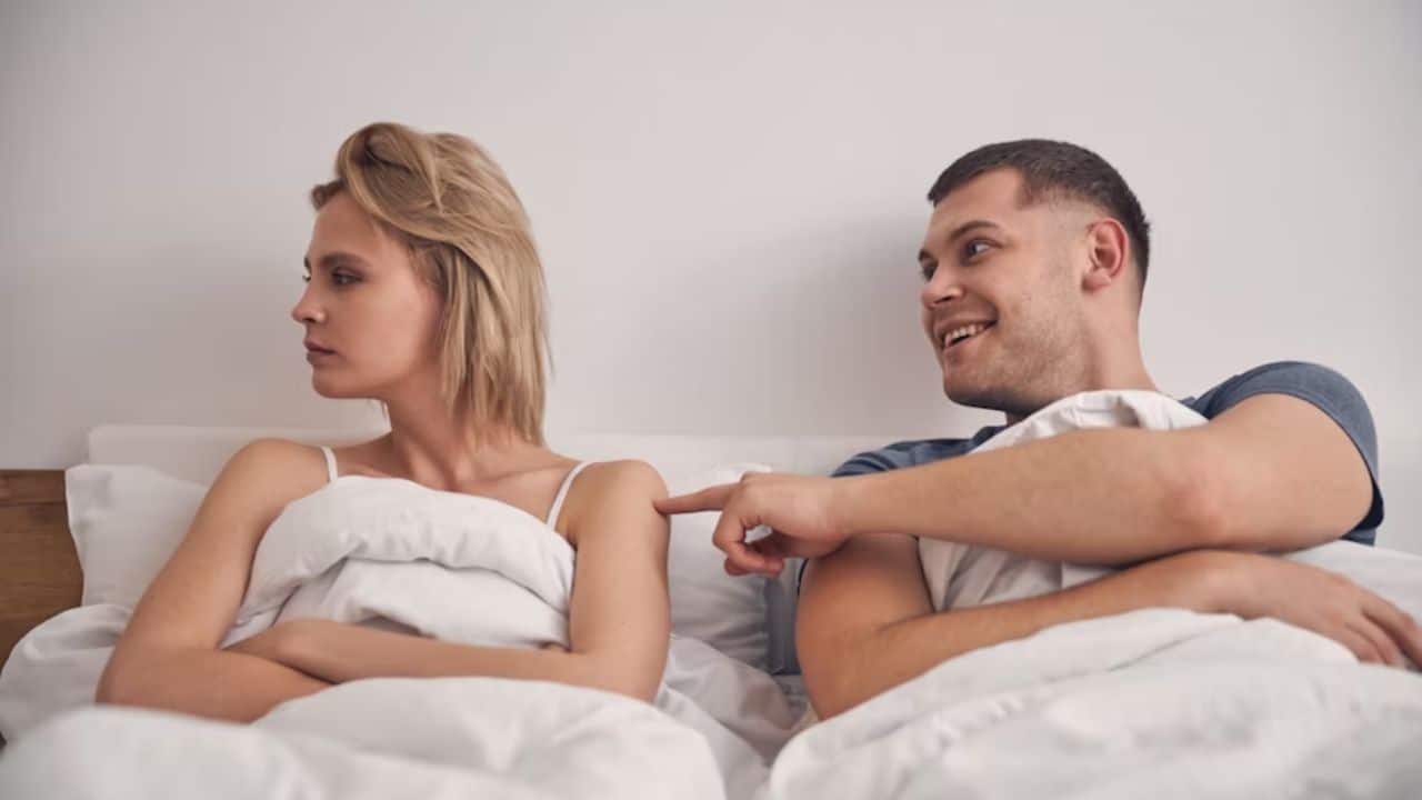 Woman angry in bed while the man is trying to make her smile.