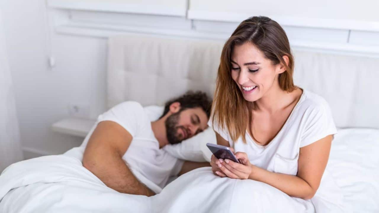 Woman looking at her phone as the man sleeps in bed.