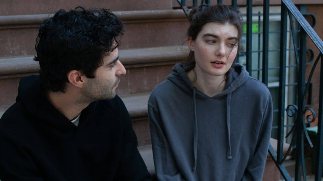 A man and woman are sitting together on a set of brownstone stairs, talking.