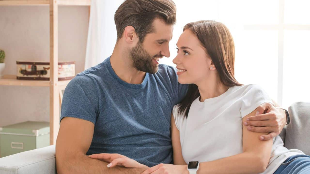 A smiling man with his arm around a woman's shoulders, looking at her and talking.